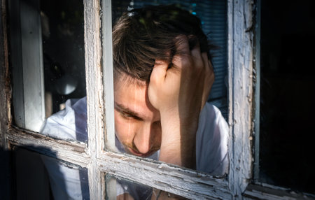 Sorrowful Young Man in the House behind the Old Windowの写真素材