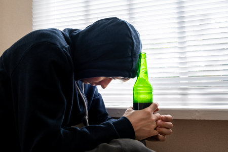 Sad Young Man with a Beer by the Window in the Roomの写真素材