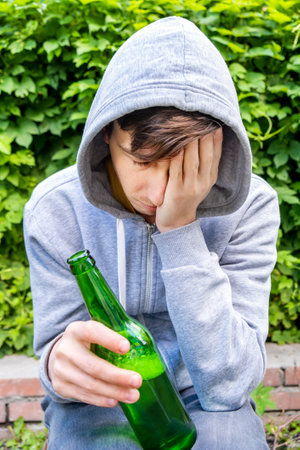 Sad Young Man in a Hoodie hold a Beer Bottle on the Green Leaves Backgroundの写真素材