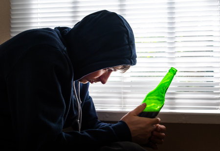 Sad Young Man with a Beer by the Window in the Roomの写真素材