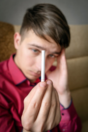 Pensive Young Man looking at a Cigarette in the Doubtの写真素材