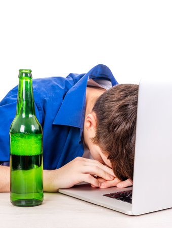Man with a Beer Bottle sleep on the Laptop Computer Isolated on the White Background closeupの写真素材