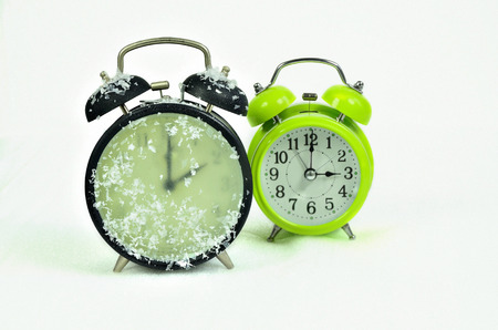 close up of two retro alarm clocks, black and green, showing wintertime and summertime, 2 am, 3 am, on white background, horizontalの写真素材