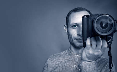 Black and white image of photographer taking a photo with digital 85mm lens reflex camera. caucasian Man taking photo of you with mirror camera. photographer with lens in hand on gray backgroundの写真素材