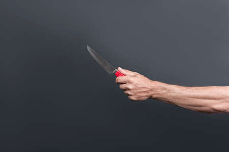 Rusty old knife with a red handle in the male hand. With space for an inscription. Kitchen meat knife in the hand isolated over gray background. Chief steel knife. Killer man holding knife in handの写真素材