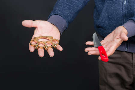 Brass knuckles and knife on the man`s palm. Metal brass knuckles in the hand of American man. forbidden weapons in a fight, criminal. caucasian man holds and shows a brass knuckles with two handsの写真素材