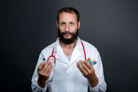 bearded Caucasian American doctor wearing doctor uniform and stethoscope holds a test tubes to send to the laboratory for blood analysis. The taking of biological material to identify the virus, fluの写真素材