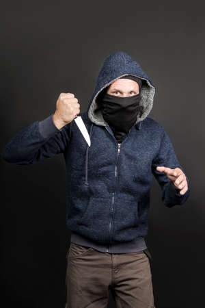 American hooded man with black mask holding knife and looking at the camera. Robbery, violence and economic crisis concept. Caucasian maniac, thief, gangster and a rapist attack with knife. Copy spaceの写真素材