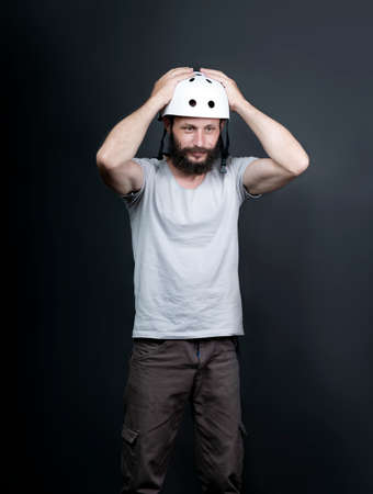 Shocked American handsome bearded man in a bicycle protective helmet standing and holds his hands on his head. Russian biker with a white helmet on his head slides it off. Surprised look, expressingの写真素材