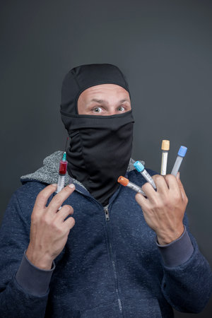 Caucasian American brutal man in blue hoodie and black face mask using syringe to suck vaccines or liquid medicine out of vial bottle. Crazy doctor holding syringe with injection. virus vaccineの写真素材
