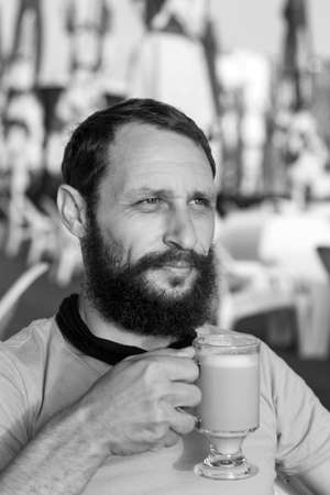 Black and white portrait of handsome bearded man drinking hot, morning espresso coffee with milk looks into the distance In sunset lighting. concept with space for text. Man Holding A Coffee Mugの写真素材