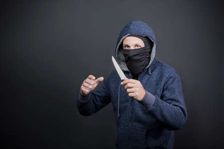American hooded man with black mask holding knife and hand reaching, grabbing or attacking. Robbery, violence and economic crisis concept. Caucasian maniac, thief, gangster, rapist attack with knifeの写真素材