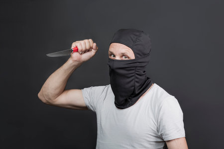 Metal knife in the hand of caucasian man in black mask. The criminal with a knife weapon threatens to kill. With space for an inscription. News staties, newspaper, social issues. american manの写真素材