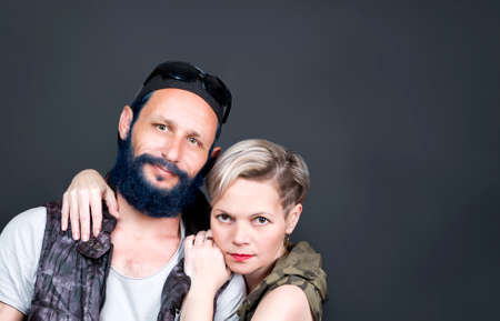 Studio portrait of american handsome man with blue beard wearing a cap, sunglasses, hoody vest and Russian woman blonde hair are standing next to each other, posing for camera. Fairy tale man, killerの写真素材