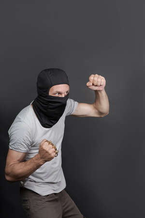 an offender attack with Brass knuckles. Metal brass knuckles in the hand of caucasian man in black mask. forbidden weapons in a fight, criminal. american man showing fist with brass knuckles. close upの写真素材