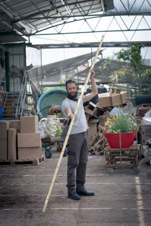 Portrait of American Caucasian bearded man buying bamboo in hypermarket, garden center. Russian buyer chooses decorative fence from bamboo in wood store. Israeli Man holding a bamboo log in handsの写真素材