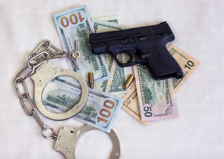 Pistol gun and bullets 9mm ammunition, handcuffs and American dollar banknotes on white background. Criminal money and punishment, top view, Copy space for text. us dollars, Financial Crime Bannerの写真素材