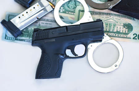 Pistol gun and bullets 9mm ammunition, handcuffs and American dollar banknotes on white background. Criminal money and punishment, top view, Copy space for text. us dollars, Financial Crime Bannerの写真素材