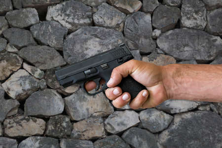 Hand holding gun against a stone wall. Close-up view Legendary US Army Pistol In arm. Cropped Image Of Man hold a 9 mm hand gun with bullets. High quality photo, copy space. Studio photoの写真素材