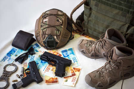 Military uniform and equipment, ammunition. Body armor, guns, bulletproof helmet, handcuffs, sunglasses and military boots with banknotes of Israeli New Shekels. Weapons for airsoft and urban protestsの写真素材