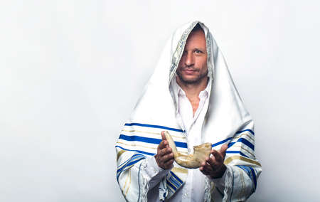 Jew man wrapped in a Tallit, prayer shawl holding the Shofar (horn). Rosh hashanah (Jewish New Year), Shabbat and Yom kippur concept. A rabbi giving a shofar in his hand, before the Tishrei holidaysの写真素材