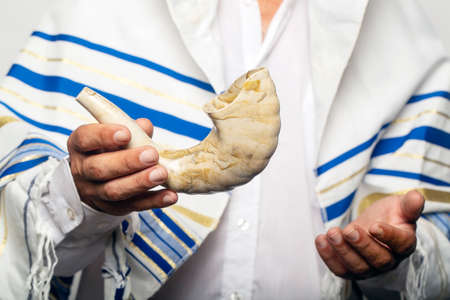 Jew man wrapped in a Tallit, prayer shawl holding the Shofar (horn). Rosh hashanah (Jewish New Year), Shabbat and Yom kippur concept. A rabbi giving a shofar in his hand, before the Tishrei holidaysの写真素材