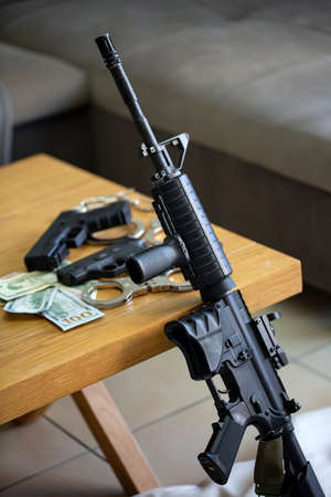 Modern automatic high powered rifle, police handcuffs, semi automatic handgun pistol, gun firearm with mags and US american dollar banknotes on wooden table. Crime, mafia, Terrorism, selective focusの写真素材