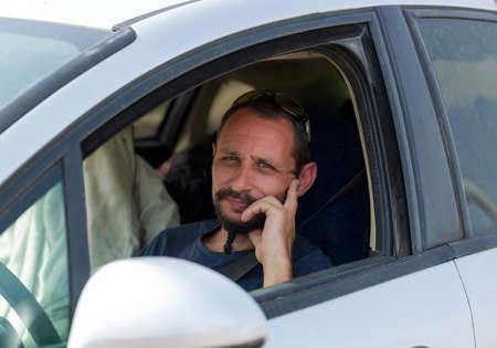 The beard caucasian man is alone driving a white car. Seen from the window of a male driver while...
