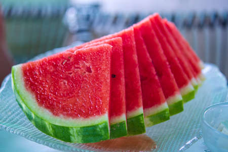 Selective focus of watermelon in glass plate on desk. Fresh sliced into triangles watermelons on a plate in summer time. Red slices on the transparent dish. Cut slices of juicy watermelon on tableの写真素材