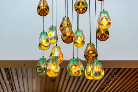 Rain drop glass pendant lights hanging from the ceiling. Ceiling glass balls living room interior decoration. Light bulb glowing hanging in rows on long wires, cords. Lighting lamps on the chandelierの写真素材