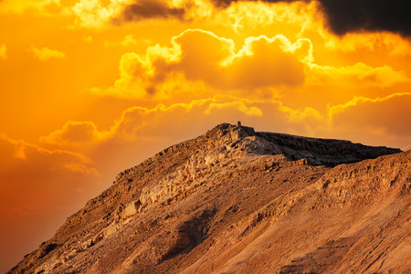 Dramatic evening gold sunset sky over mountain Sodom Gomorrah from Negev desert, Israel, Dead sea. Sunset on a foggy mountains range Sodom with fluffy clouds. Sun shining on rocky landscape in the hillsの写真素材