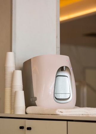 Modern water cooler with glass plugged into wall in office. Space for text. Freshy cold and hot drinking water in cooler on wooden table in kitchen. Kitchen area in the office. pink water coolersの写真素材