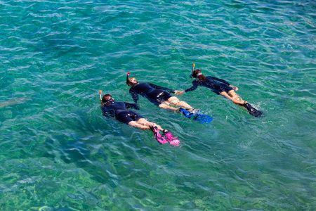 Three female divers with scuba masks and flippers diving in crystal clear water in Eilat, Red sea, Israel. Divers are training at the sea. Young girl diver in black scuba diving suits playing in waterの写真素材