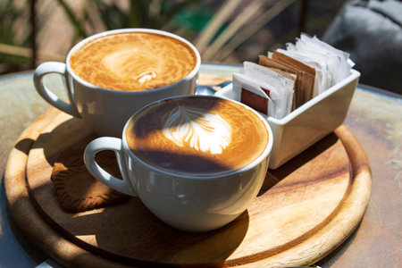 Two cups of cappuccino with latte art on wooden table in the morning in direct sunlight. selective focus. Inspirational early morning breakfast with coffee. Espresso, latte coffee cups on wood trayの写真素材