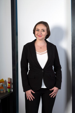 Lovable brunette lady standing in black suit looking at camera with an enigmatic smile. Beautiful elegant professional woman in a stylish jacket. Beautiful stylish woman standing near window in officeの写真素材