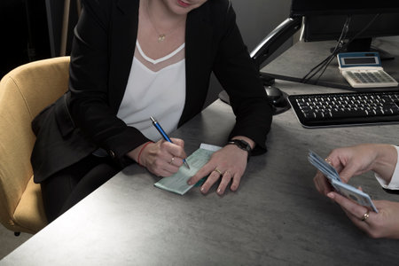 Attractive young Israeli caucasian woman working on finances at office wearing black jacket sitting at work table. Woman hand filling checks, paying bills and doing banking. Writing bank checkの写真素材
