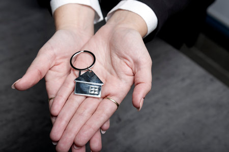 Caucasian woman's palms points at the keys with keychain in her hand. Agent's businesswoman palm holds key and home shaped keychain. House key in woman's hands. Real estate, moving home or rentingの写真素材