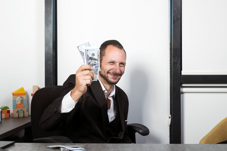 Sly Bearded Charming Jewish man in Yarmulke and formal wear sit at desk takes cash. Happy excited...