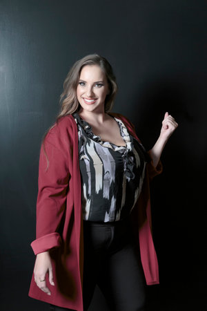 Plus size attractive lady posing and standing against dark backdrop with charming smile. Perfect makeup, fashion beauty portrait. Beautiful smiling brunette big size woman with brown long hair.の写真素材