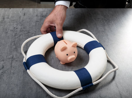 Male hand with little piggy bank inside of lifebuoy. safe money. Blue and white life buoy on wooden desk table background. Asset wealth, money saving and security by insurance concept. copyspace.の写真素材