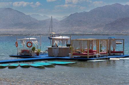 Traditional floating restaurants on the coast Israel. Empty floating restaurant and bar on Red sea at sunset. Surfboards on blue water. Travel adventure, water sport with sea and blue sky backgroundの写真素材