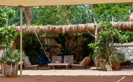 Summer thatched gazebo on a hot sandy beach. Tropical gazebo or bungalow from the sun with a sofa, garden furniture and coffee table for relaxing. Wooden canopy or tropical hut with thatched roof.の写真素材