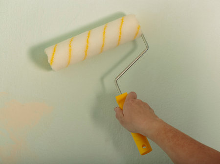 Woman using paint roller with a yellow handle. Building, renovation and construction work. Tools for painting walls. Human Hand holding new roller brush. A men hand hold paint roller and painting wallの写真素材