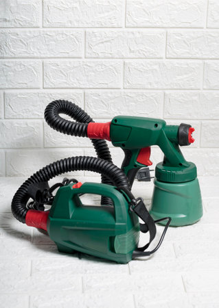 Electric green colored paint sprayer over a white brick background. Useful Instrument for quick paint jobs. New spray gun technology used by professionals, clean and efficient device for renovationの写真素材