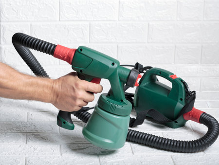 Male hand holds electric green colored paint sprayer over a white brick background. Useful Instrument for quick paint jobs. New spray gun technology used by professionals. paint spray gun in handの写真素材