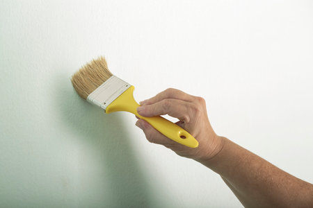 Cropped hands of woman painting with brush painting wall repair. Woman testing paintbrush with a yellow handle. Concept creative design house interior. Woman's hand brushing, painting white a wall.の写真素材