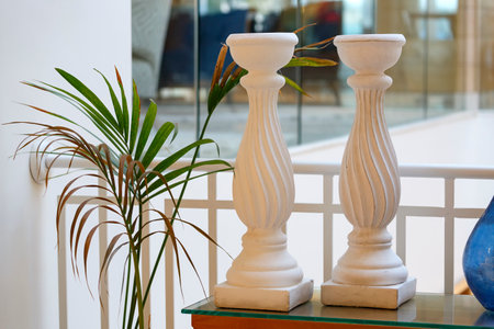 Two large white wooden candle holder stand on the table as part of table decoration and green leaves, decor. Decorative candlesticks on a stand against the background of the white wall and green plantの写真素材