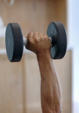 Dumbbell in man's hand on a blur background, working on muscular endurance. A muscular male hand holds out, lifting a heavy dumbbell in the gym. Cropped photo of a strong man holding dumbbell in handの写真素材