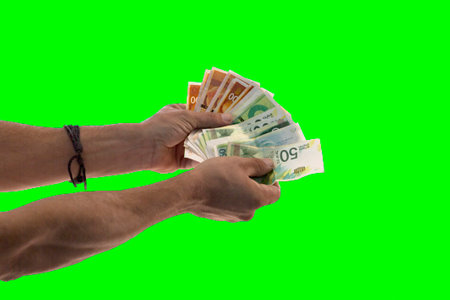Man hands displaying spread of cash over a green background. Money saving concept. Businessman hand holding a bundle of money, new Israeli shekel banknotes on green chroma key background, patternの写真素材
