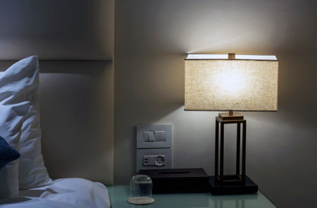 Lamp on bedside table in contemporary style white room interior with bed, pillows and white cotton bedlinen. Bedroom interior elements. Bedside table lamp in modern contemporary styleon night table.の写真素材